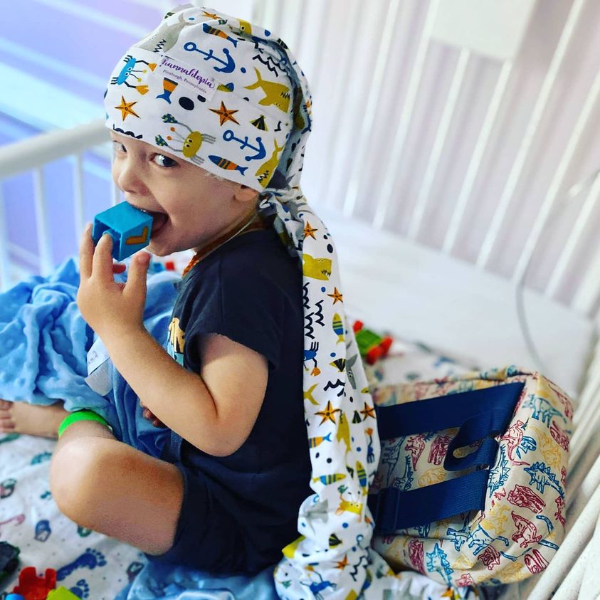 boy putting blue block to his mouth during eeg while wearing the shark nillynoggin eeg cap