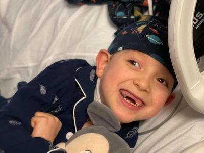 boy smiling in hospital bed during EEG wearing planets NillyNoggin EEG Cap