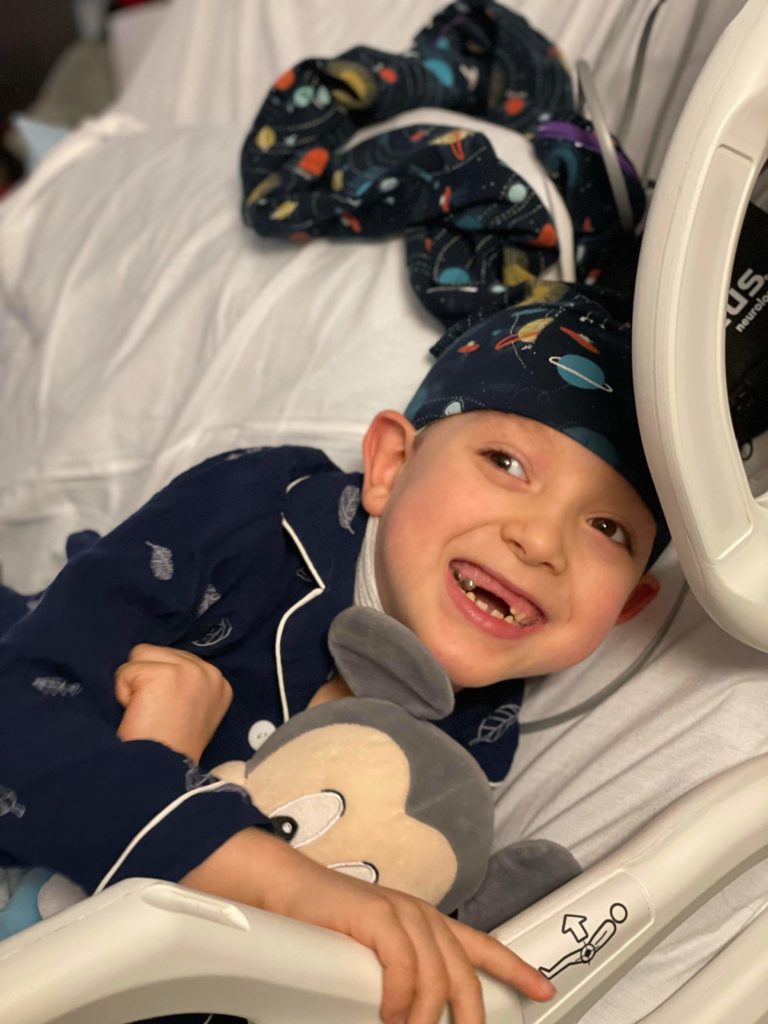 boy smiling in hospital bed during EEG wearing planets NillyNoggin EEG Cap